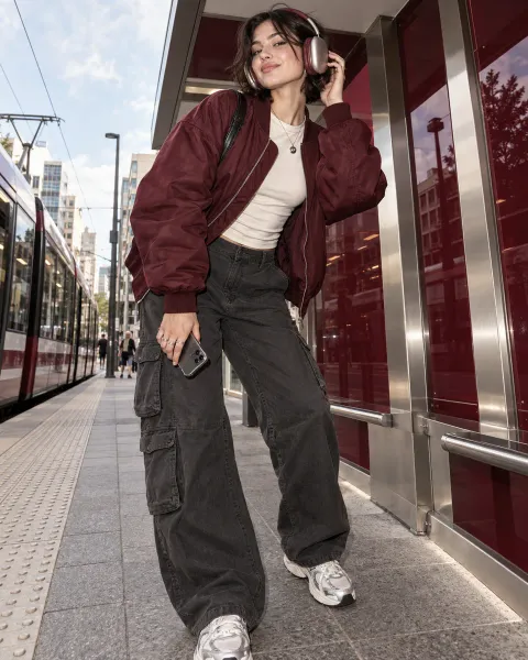 Young adult wearing SONORA headphones with contemporary burgundy streetwear at an urban tram stop
